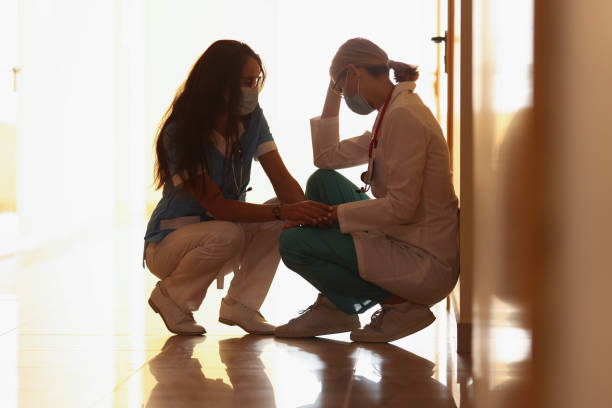 Low angle of tired medical worker after hard long surgery sitting on floor. Nurse support colleague doctor. Medicine, save life, health, tragedy concept